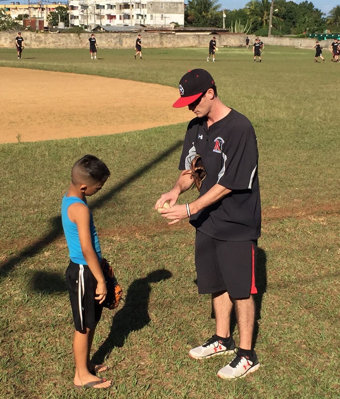 A coach handing a baseball glove to a young player at the edge of a field