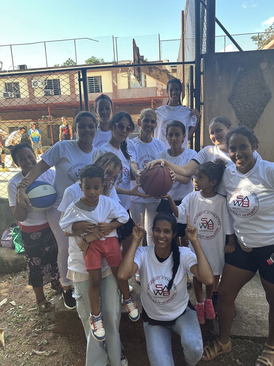 A group in matching clinic shirts gathered around a basketball on an outdoor court