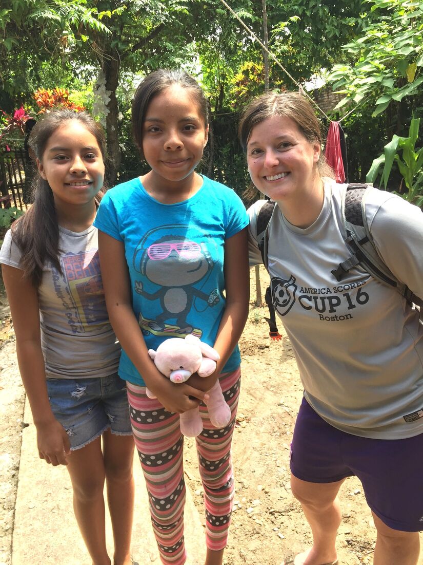 Two children holding a stuffed toy on a dirt path beside a smiling adult