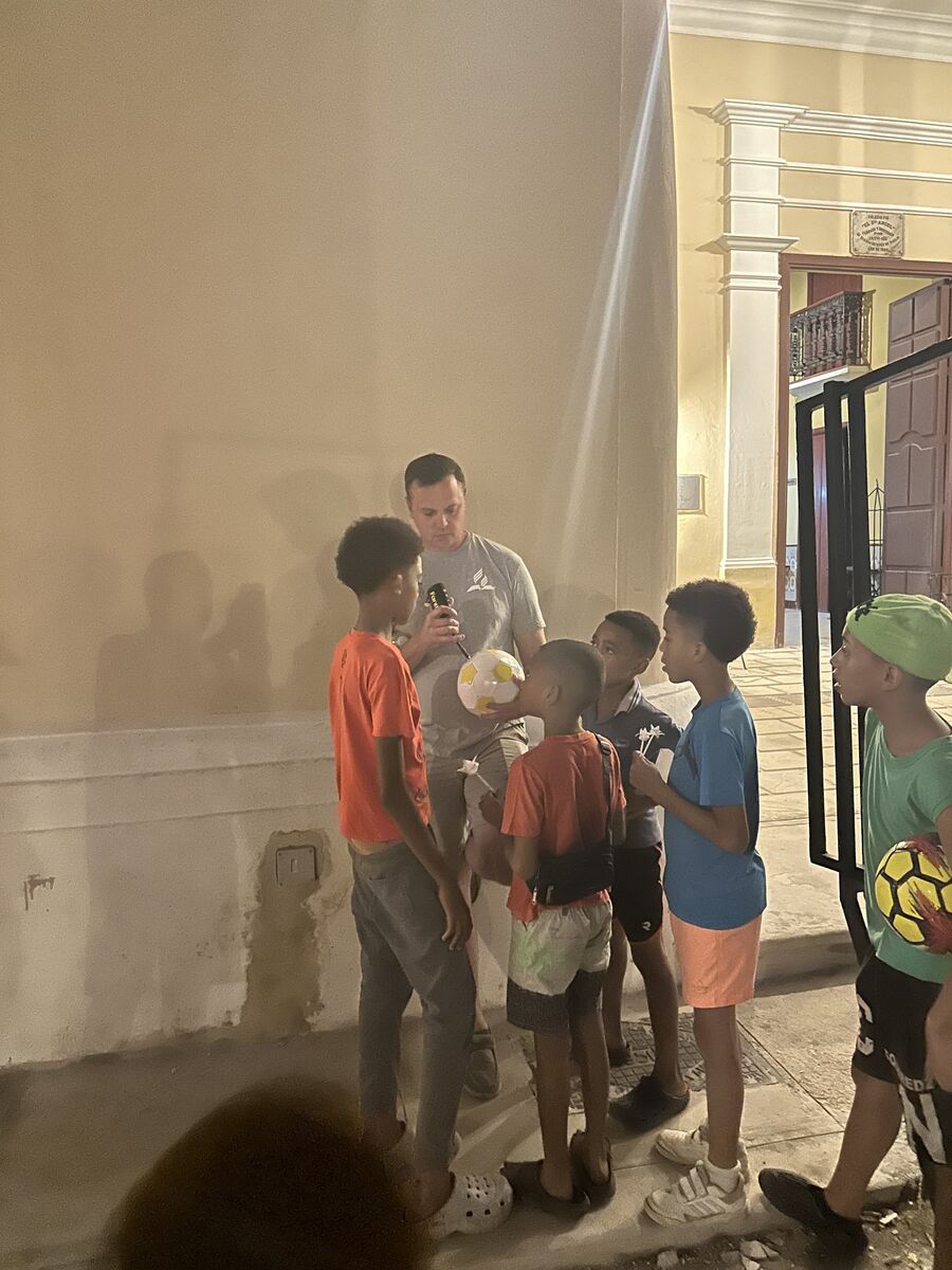 Children holding a soccer ball in a sunlit doorway with an adult beside them
