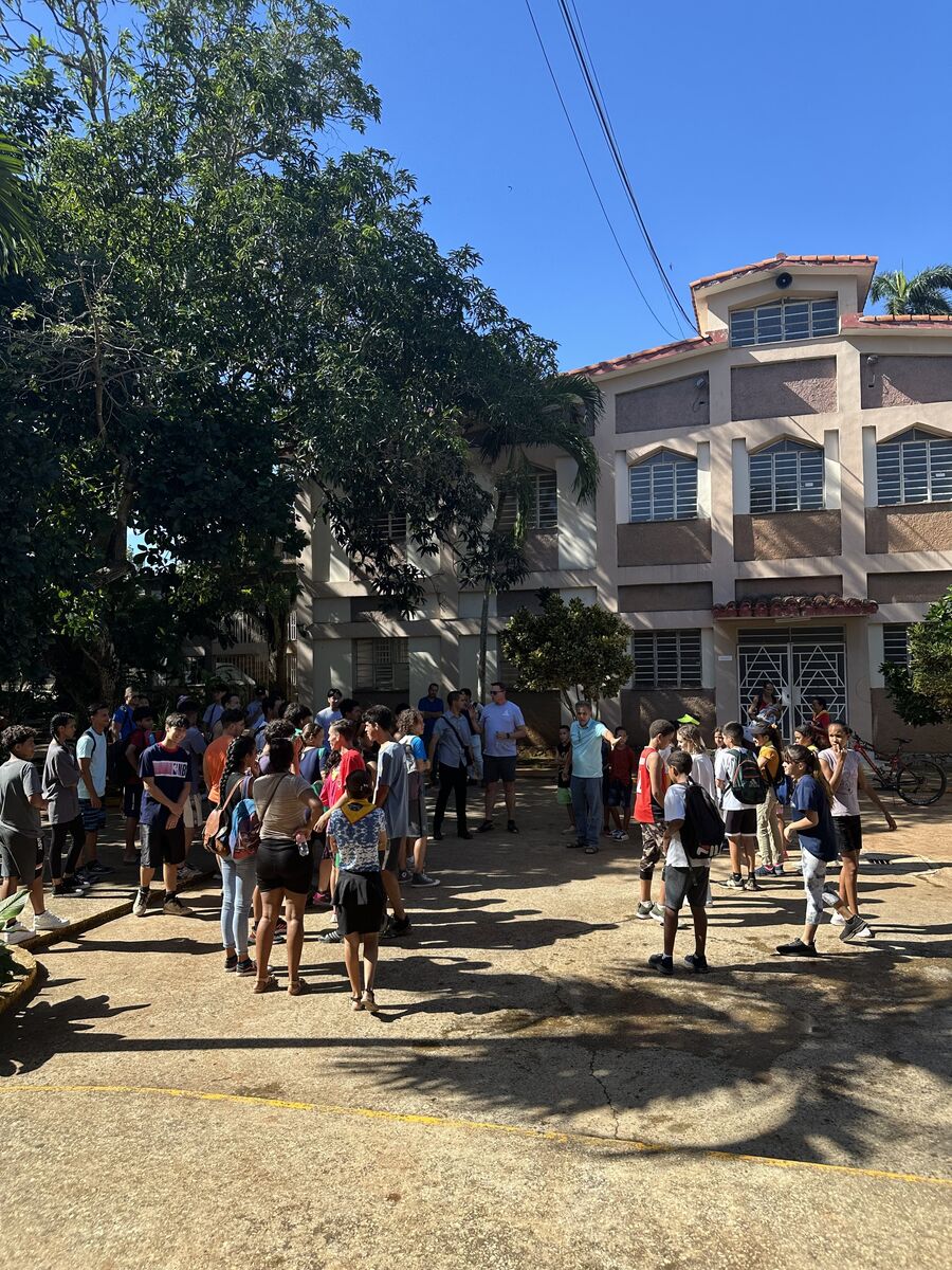 Dozens of young athletes and adults gathered on a shaded street outside apartment buildings