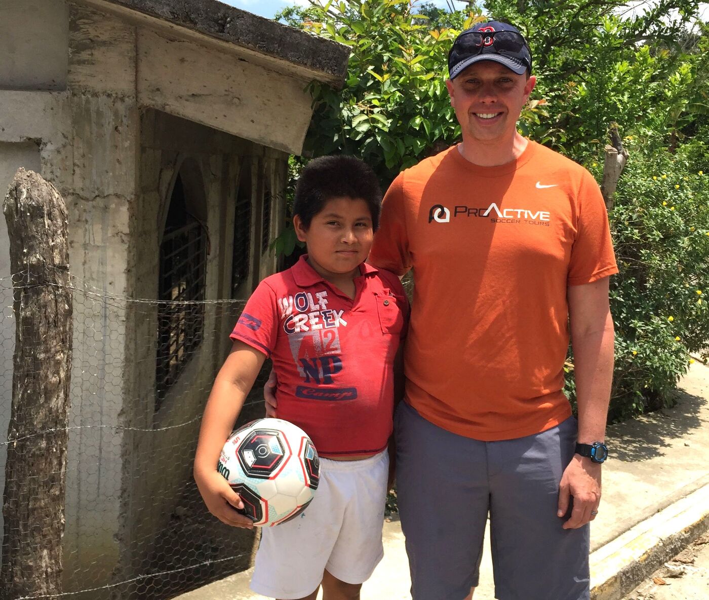 A young player holding a soccer ball beside a coach outside a home
